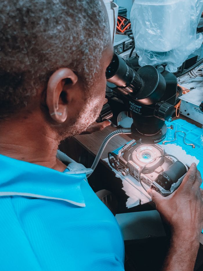 A skilled technician examines and repairs a device using a microscope in a workshop setting.